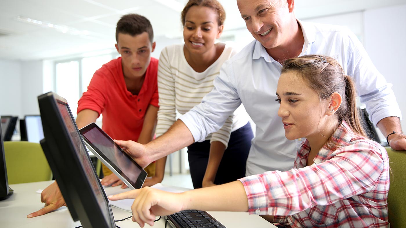 Schüler und Lehrer eines Berufsbildungswerks schauen gemeinsam lächelnd auf den Monitor