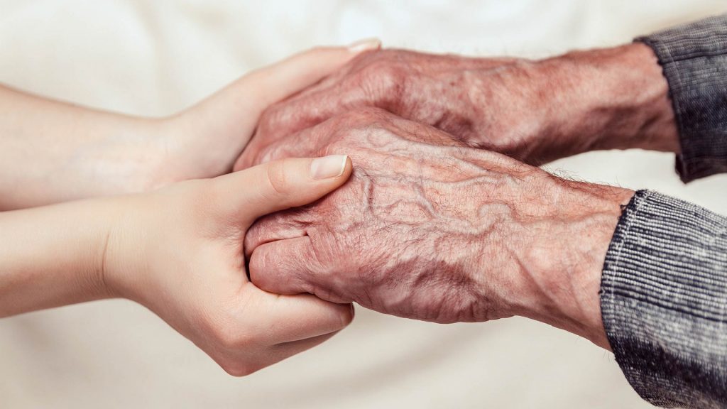 Hände eines alten Mannes und einer jungen Frau halten einander vertrauensvoll