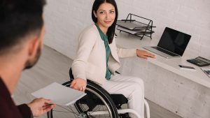Rollstuhlfahrende Arbeitgeberin übergibt ihrem Assistenten ein Arbeitsdokument