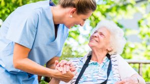 Altenpflegerin umgreift vertrauensvoll die Hand einer Seniorin im Rollstuhl