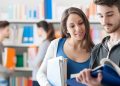 Zwei Studierende schauen in der Bibliothek gemeinsam glücklich in ein Buch