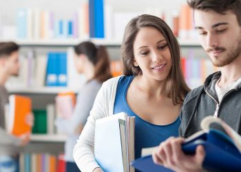 Zwei Studierende schauen in der Bibliothek gemeinsam glücklich in ein Buch